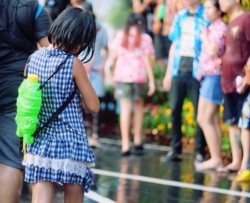 Rear view of girl with squirt gun standing on footpath during buddhist new year
