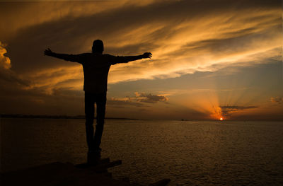 Rear view of man standing on beach against sunset sky