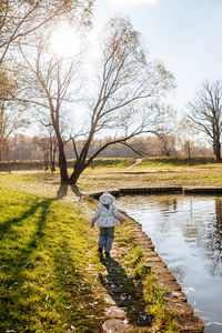 Rear view of little girl walking across lake against sky