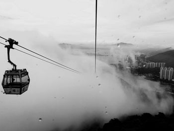 Overhead cable car moving towards clouds against sky