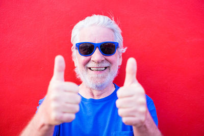 Portrait of senior man wearing sunglasses gesturing against red background