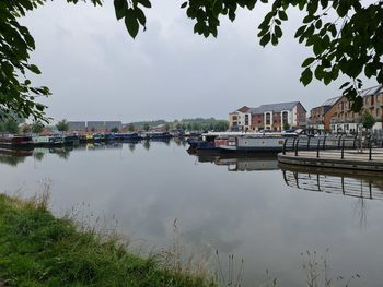 Sailboats moored on lake by buildings against sky