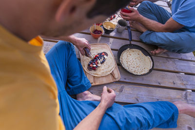 Man pouring maple syrup on sweet crepe sitting on wooden structure