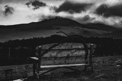 Abandoned bench on field by mountain against sky