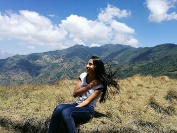 Young woman sitting on mountain against sky