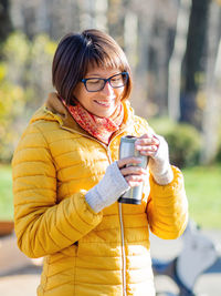 Happy wide smiling women in bright yellow jacket is holding thermos mug. hot tea at  autumn day.