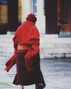 Rear view of woman with red umbrella walking in city