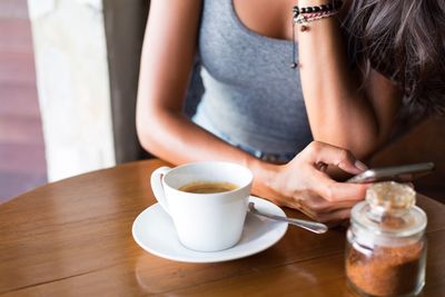 Midsection of woman with coffee cup on table