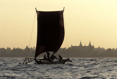 People sailing on sailboat on sea against clear sky during sunset