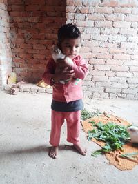 Thoughtful boy holding rabbit while standing against brick wall