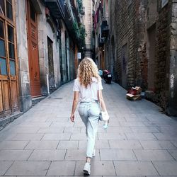 Rear view of woman on footpath amidst buildings in city