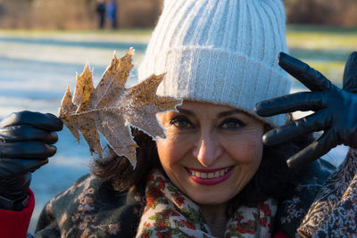 Portrait of smiling woman in warm clothing holding frozen leaf