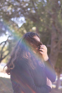 Woman covering face with hair standing against trees