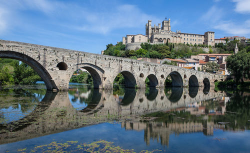 Arch bridge over river by buildings against sky