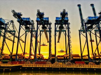 Cranes at construction site against sky during sunset