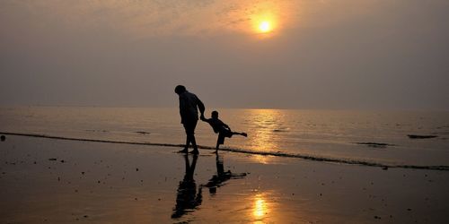 Silhouette people at beach against sky during sunset