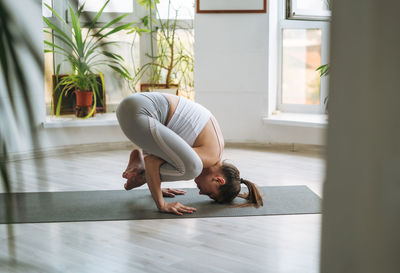 Young fit woman practice yoga doing asana in light yoga studio with green house plants