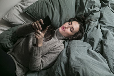 High angle view of woman using smart phone while lying on bed