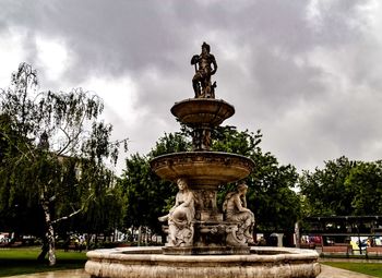 Statue by fountain against sky in park