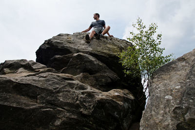 Low angle view of young man sitting on cliff against sky