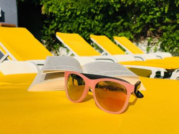 Close-up of sunglasses and book on yellow lounge chair
