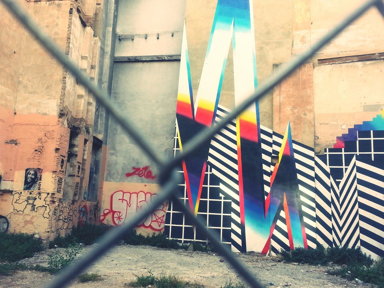 architecture, built structure, graffiti, building exterior, wall - building feature, railing, metal, protection, day, multi colored, wall, no people, safety, outdoors, sunlight, street art, chainlink fence, fence, building, security