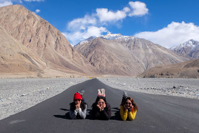 Portrait of friends lying on country road against mountain range