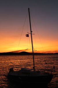 Silhouette sailboats moored on sea against orange sky