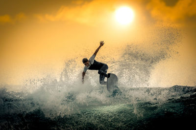 Teenager surfing in sea against sky during sunset