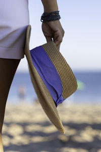 Midsection of woman holding hat at beach