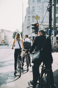 Full length of business coworkers riding bicycle on street in city