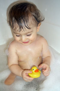 Happy little baby boy having a bubble bath with rubber duck