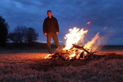 Portrait of man standing by bonfire on field against sky