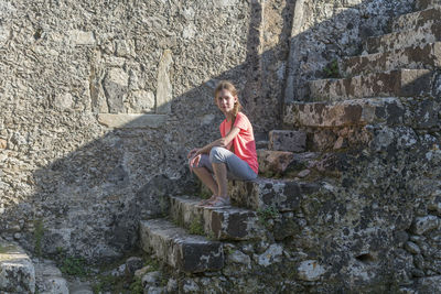 Full length of girl sitting on steps by wall