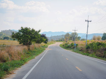 Road amidst trees and plants against sky