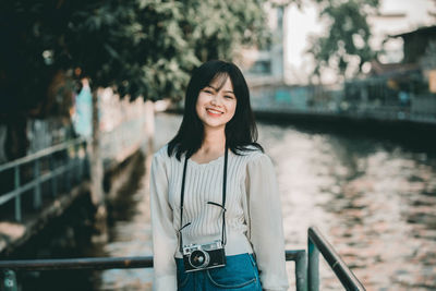 Portrait of smiling young woman standing against railing