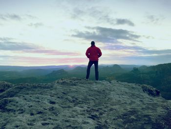 Hiker standing on a rocky mountain summit, watching the morning mist and the rising sun at dawn