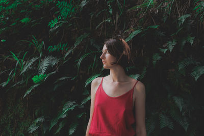 Young woman looking away while standing against plants