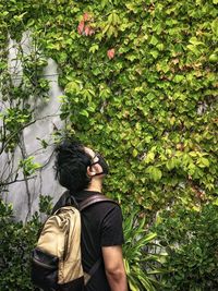 Young man standing by green, ivy covered wall.