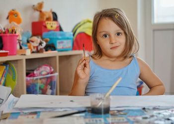 Portrait of smiling girl holding paintbrush on table at home