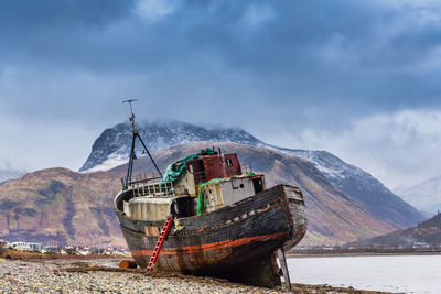 Boat moored on snowcapped mountains against sky