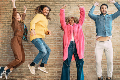 Happy friends jumping against brick wall