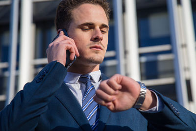 Low angle view of businessman talking on smart phone while standing against building