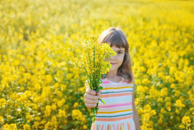 Portrait of cute girl holding flowers while standing in field