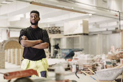 Portrait of confident male carpentry student standing arms crossed in workshop
