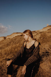 Woman sitting on field against sky