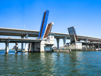 Low angle view of bridge over river against clear blue sky