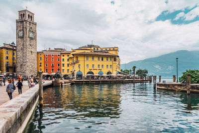 Buildings at waterfront against cloudy sky