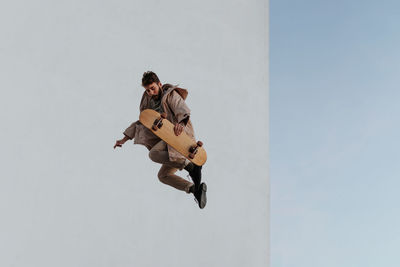 Full body young bearded active male skater in casual outfit jumping while performing trick on skateboard in skatepark