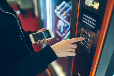 Woman paying for product at vending machine using contactless method of payment with mobile phone